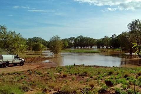 An outback crossing flooded by rainwater, with a four-wheel-drive parked at the edge of the water.