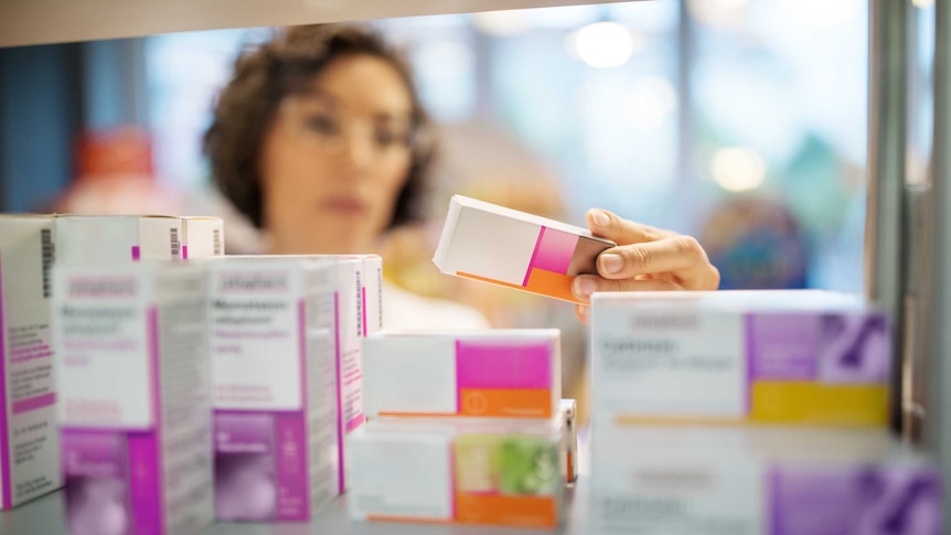 Female pharmacist checking medicines on rack.