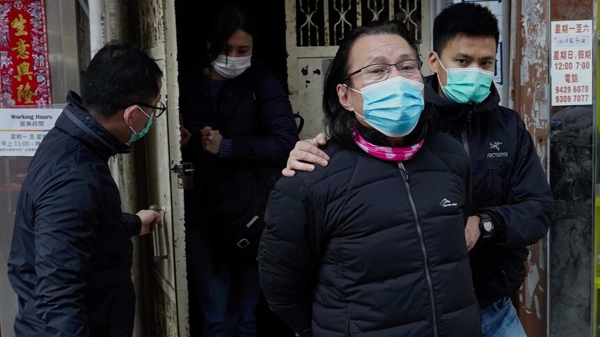 Daniel Wong Kwok-tung wearing a face mask is lead away by police as he looks at the camera