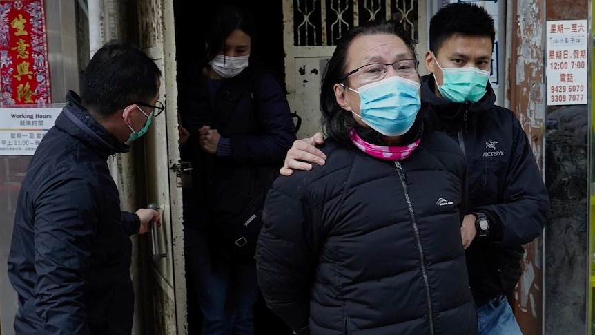 Daniel Wong Kwok-tung wearing a face mask is lead away by police as he looks at the camera