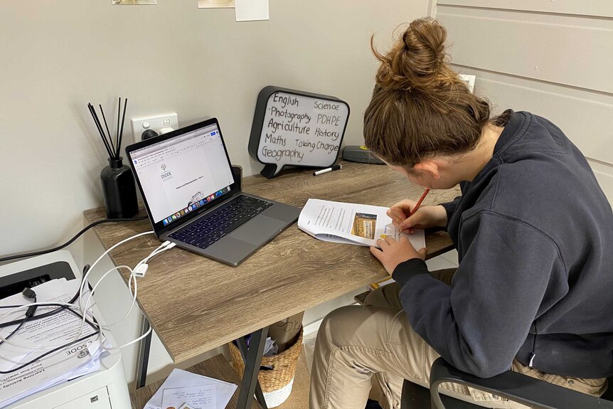 Girl with back to camera sitting at desk and writing on paper.