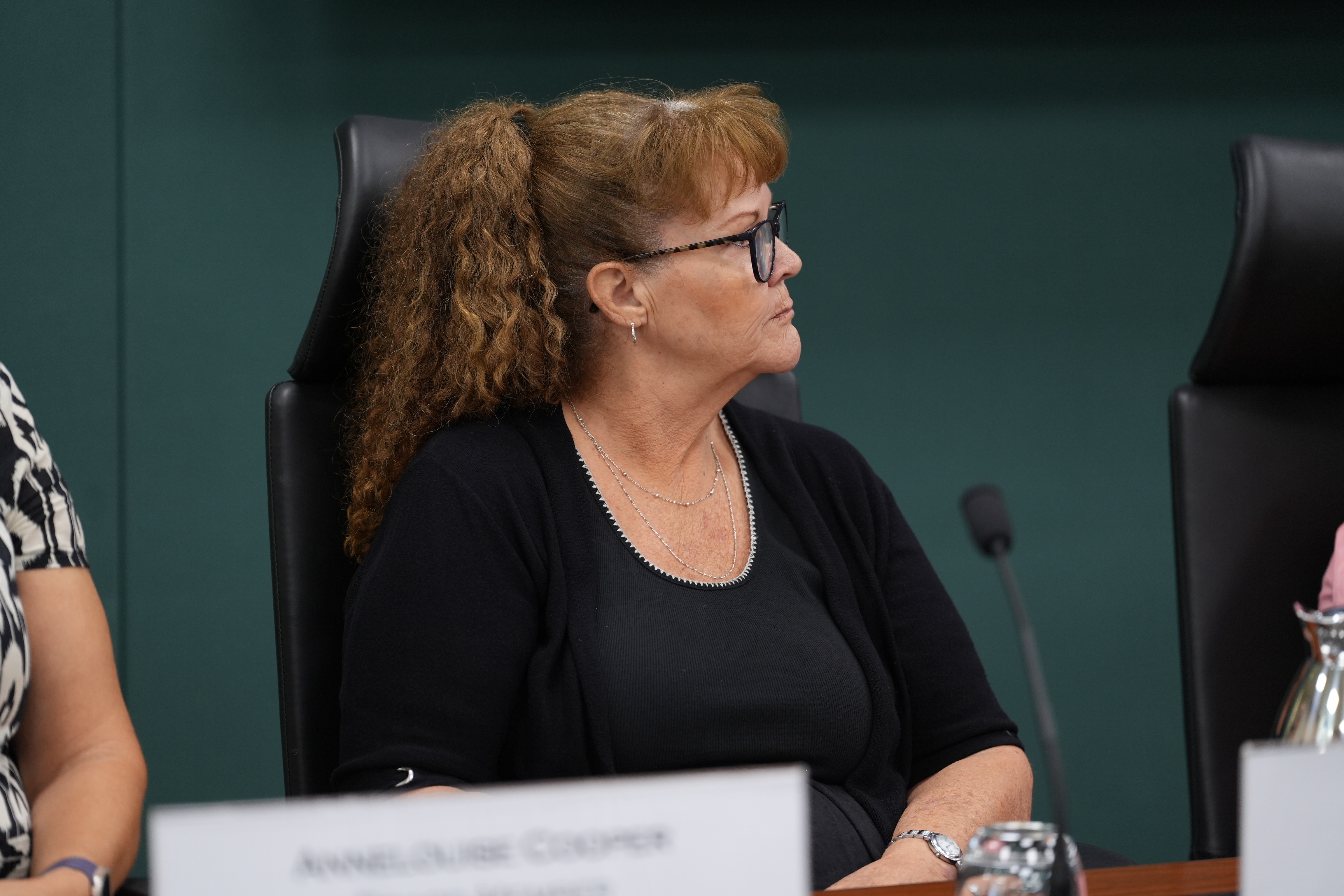 A woman with curly hair, wearing glasses while sitting before a microphone.