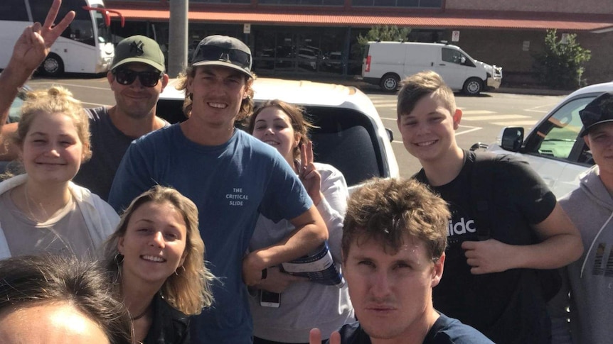 A family of nine smile in a car park in front of a shop.