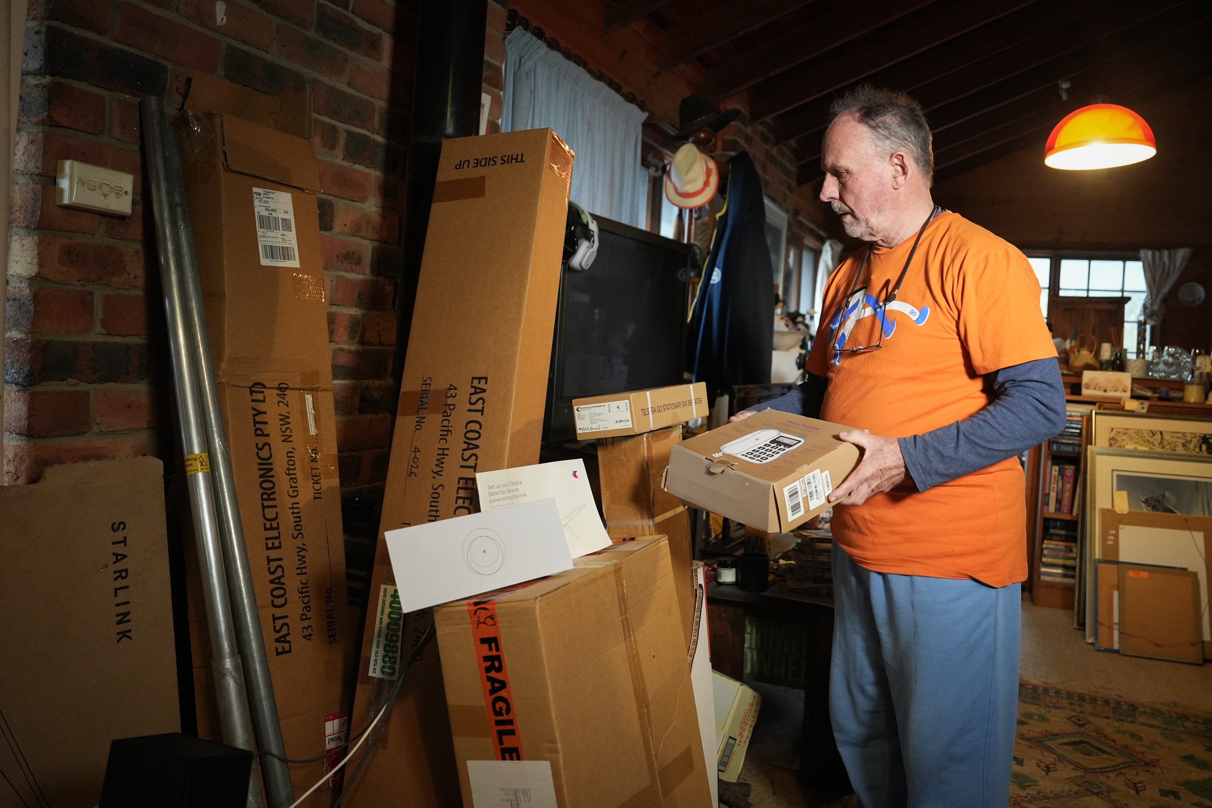 A man with short grey hair carries cardboard boxes through a house.