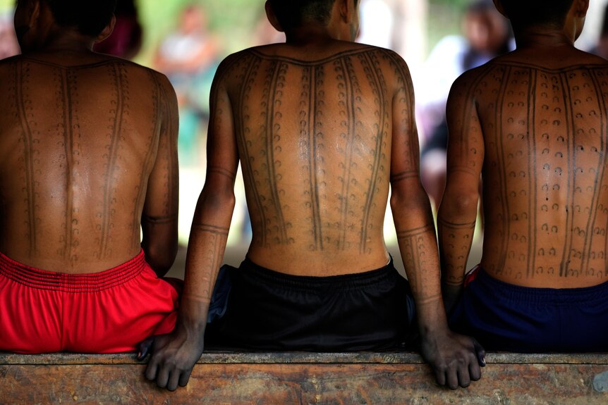 Boys have traditional designs painted in black ink up and down their backs. 