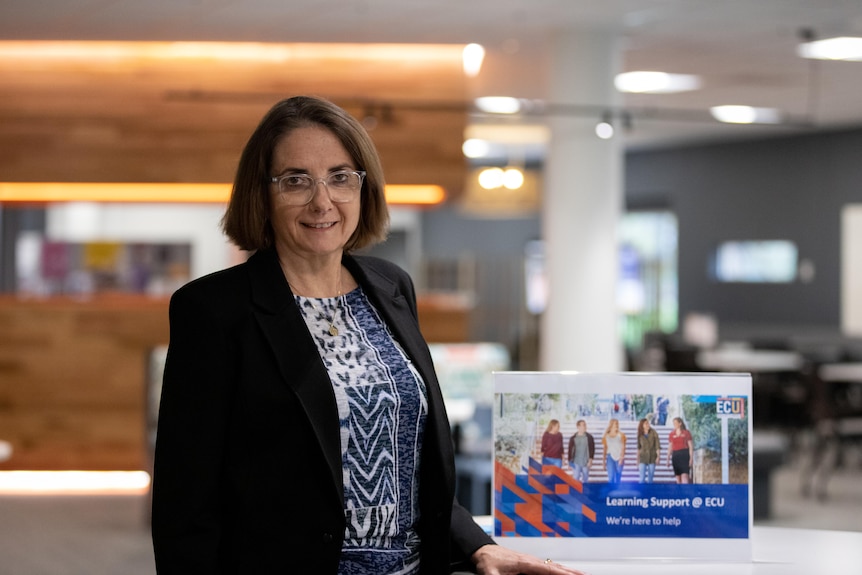 Woman stands in a library next to a plaque which says 'learning support at E-C-U'.