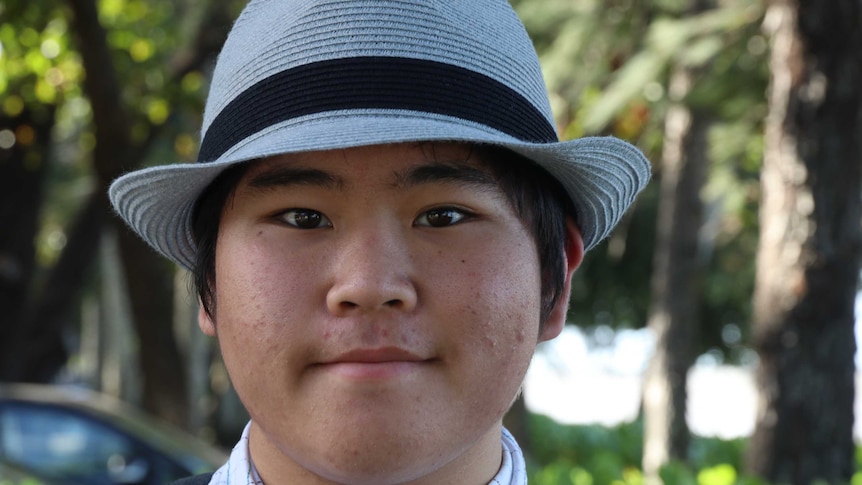 A young Japanese lad wearing a trilby-style hat looks into the camera.