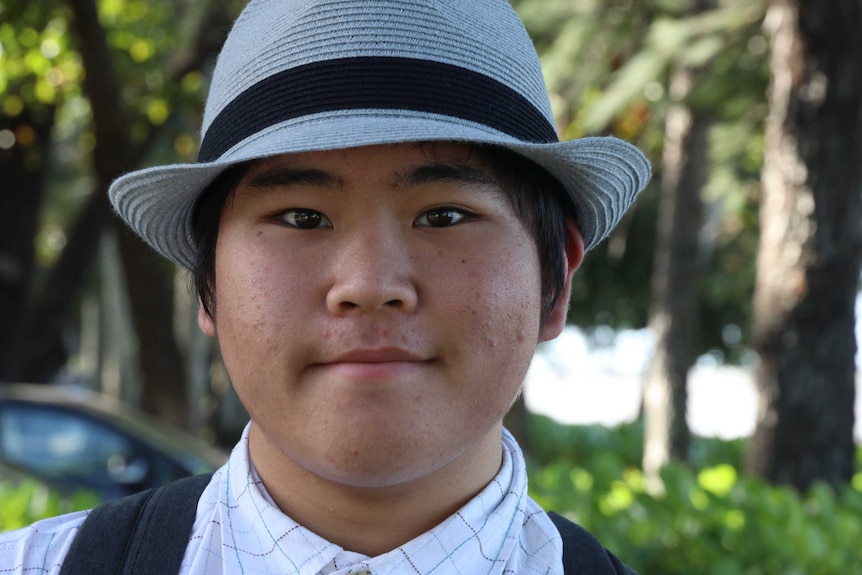 A young Japanese lad wearing a trilby-style hat looks into the camera.