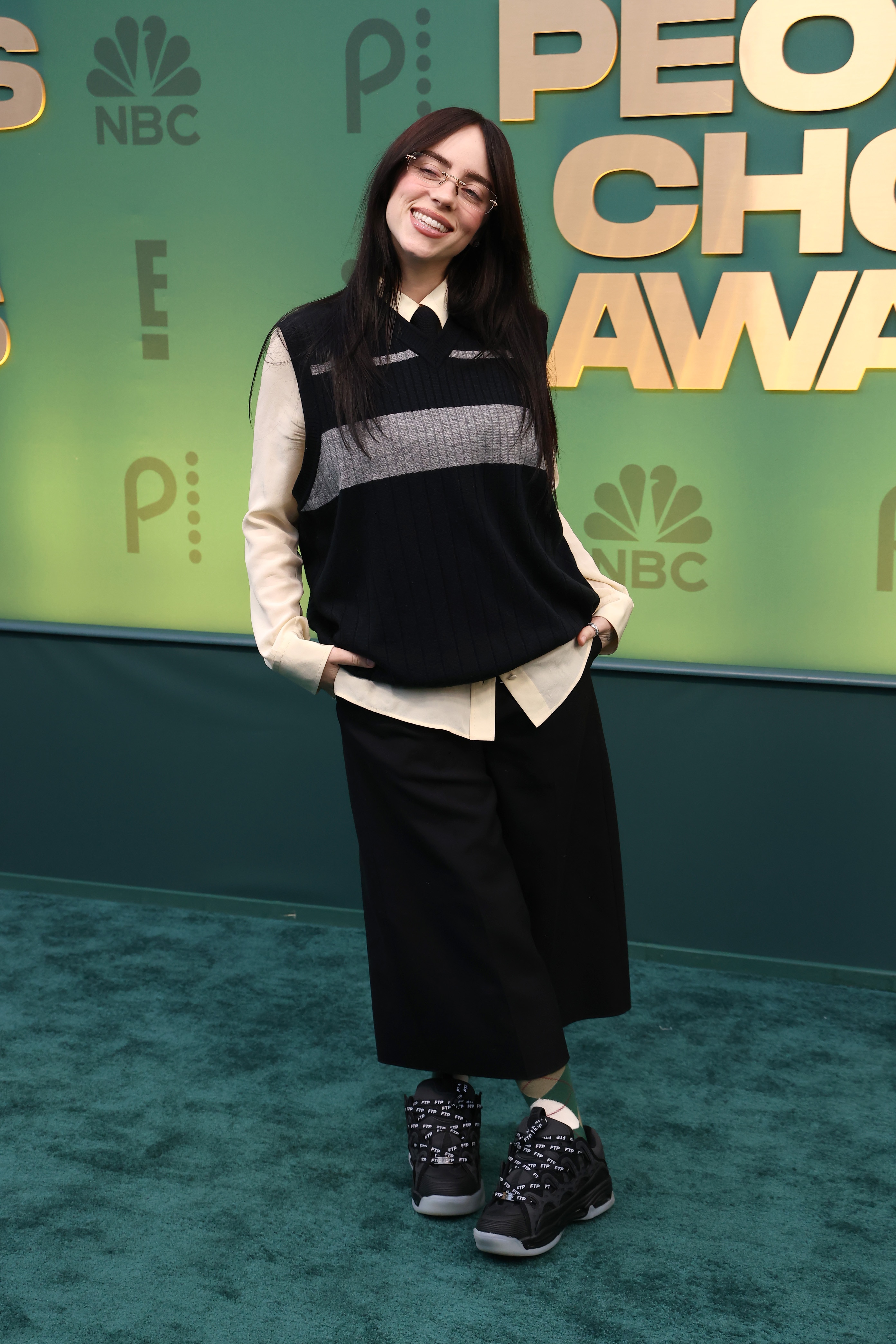 Billie Eilish on the red carpet in a black long skirt, a white collard top and black vest
