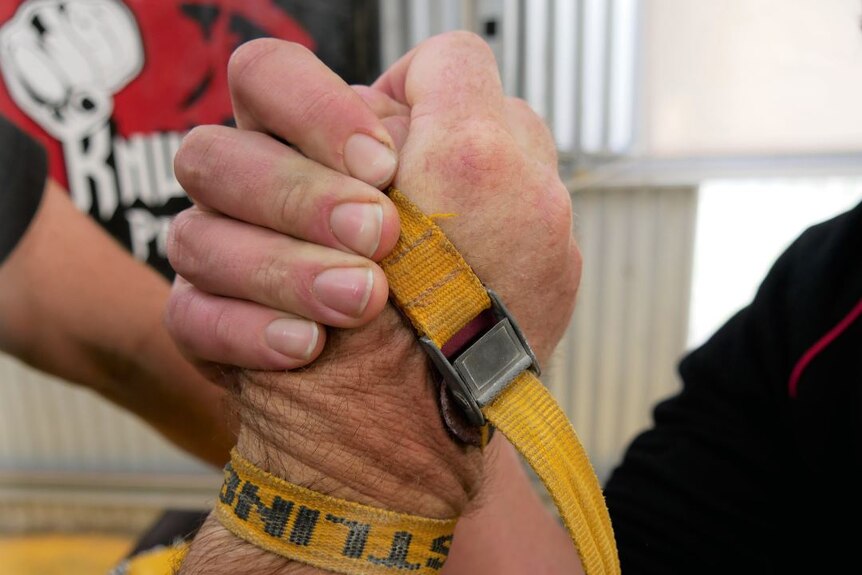 Two men grip their hands together and they are strapped with a yellow rope.