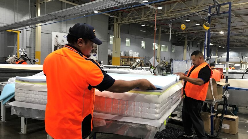 Two workers building a mattress at a factory, wearing orange, high visibility vests.