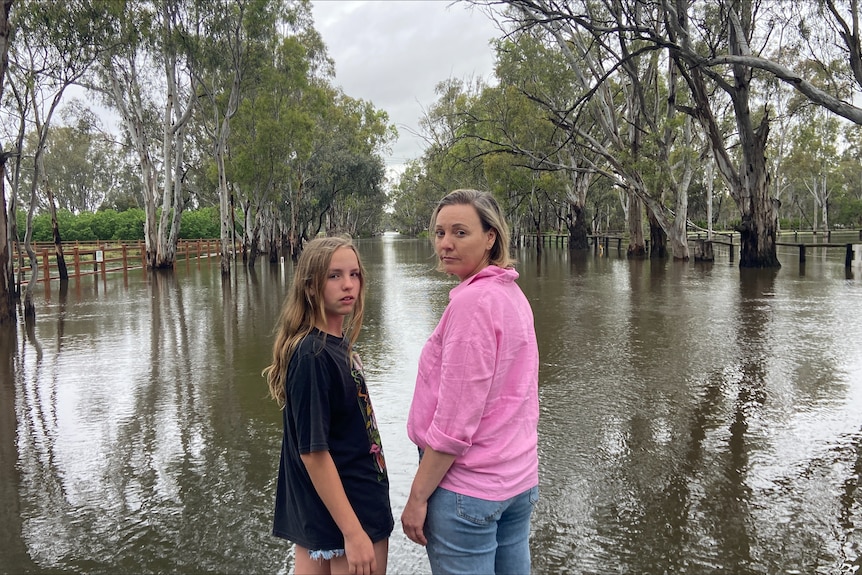 a woman and a girl look back at the camera, a flooded street in front of them
