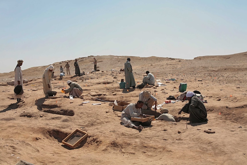 People in north African robes and head coverings dig in sandy ground.
