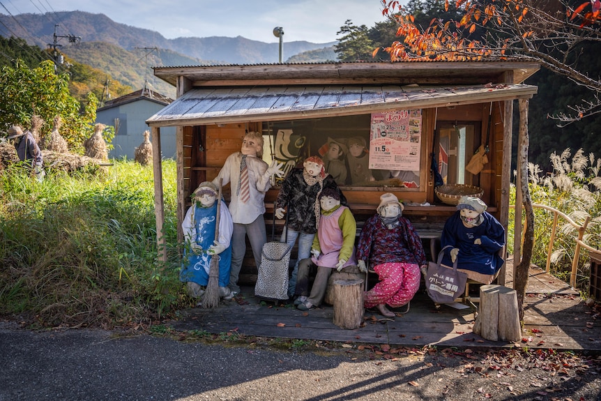 Un groupe de six poupées sont assises et rassemblées à un arrêt de bus.