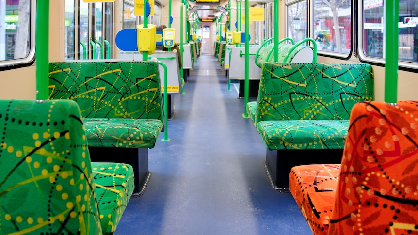 An empty tram with colourful green and orange seats, in daylight.