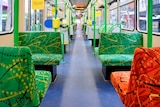 An empty tram with colourful green and orange seats, in daylight.