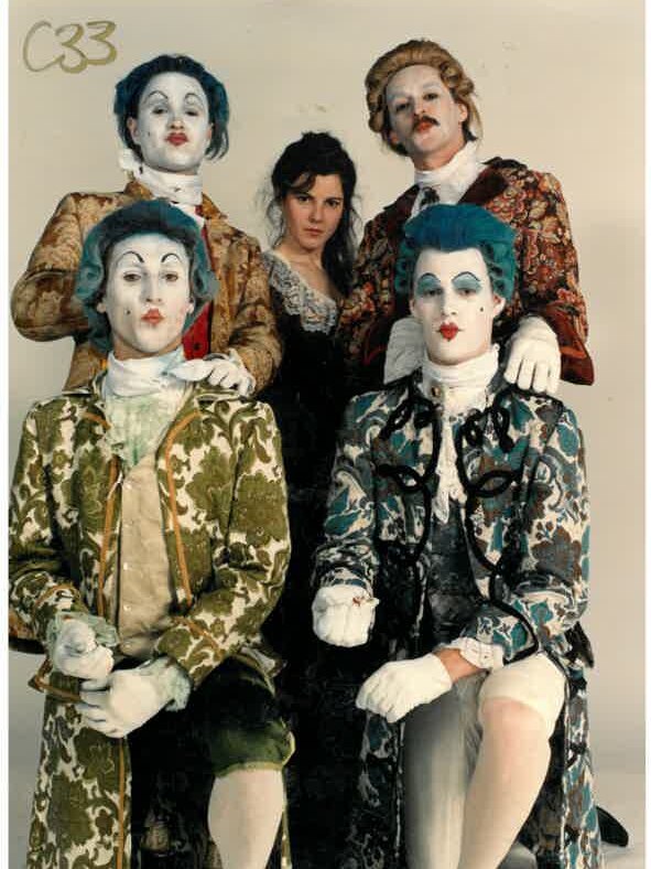 People dressed in 18th century outfits with faces painted white and wearing blue wigs