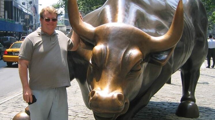 Peter Spann standing next to a bull statue on Wall Street, New York
