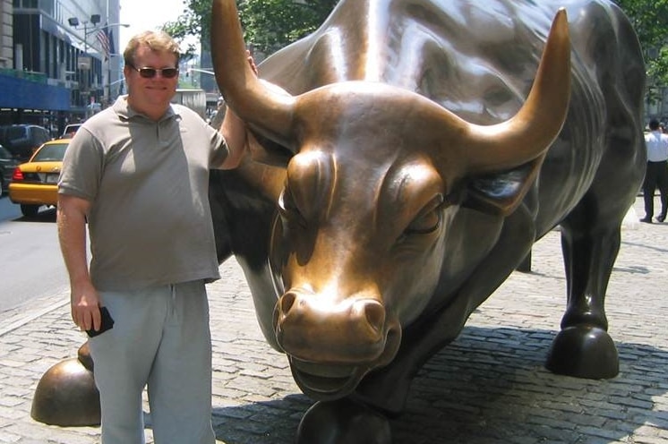 Peter Spann standing next to a bull statue on Wall Street, New York