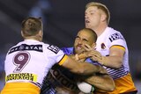 A Cronulla NRL player holds the ball as he is tackled by two Brisbane opponents.