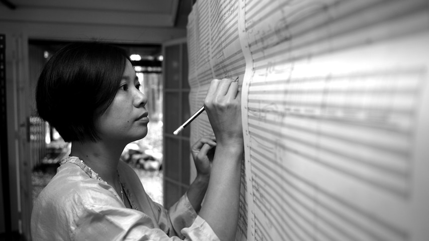 Liza Lim writes music onto large score paper pinned to a wall