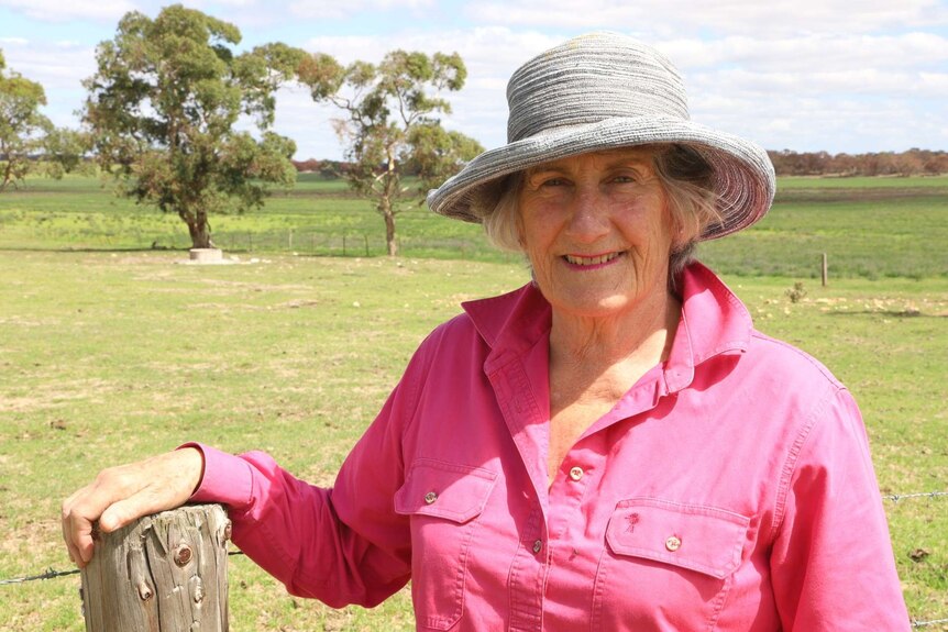 A woman in a pink shirt wearing a hat stands in front of a green paddock
