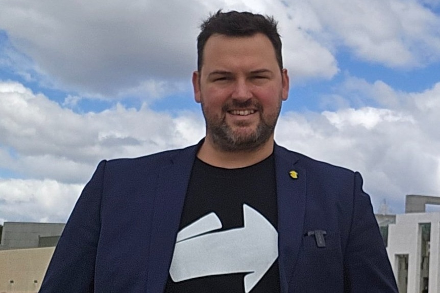 Headshot of Australian Republic Movement's Isaac Jeffrey, he wears a black shirt and blue jacket.