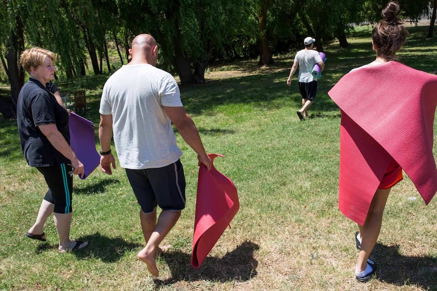 Yoga teacher Lyn Flora walks outside with several residents carrying yoga mats.