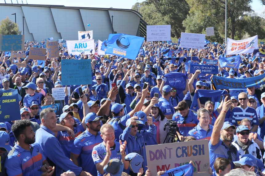 A sea of Western Force supporters holding banners and flags stands outside Rugby WA headquarters under a blue sky.