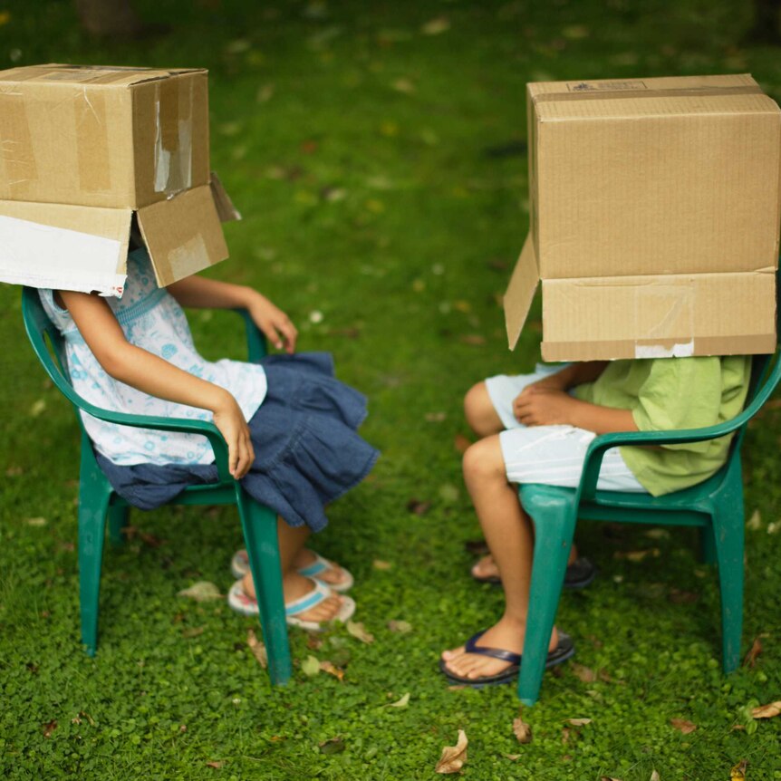Children sitting on chairs with boxes over their heads
