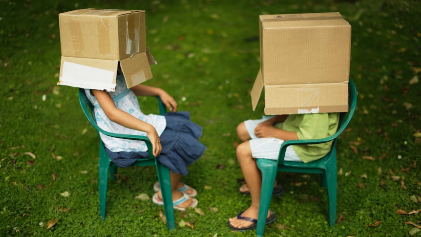 Children sitting on chairs with boxes over their heads