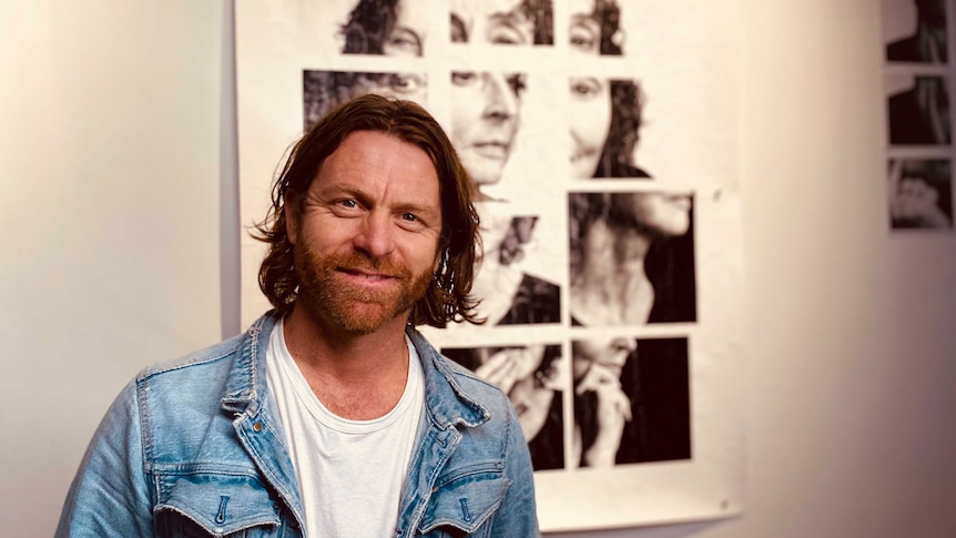 headshot of a man with beard, long hair and denim jacket standing in front of a fractured photo of a woman