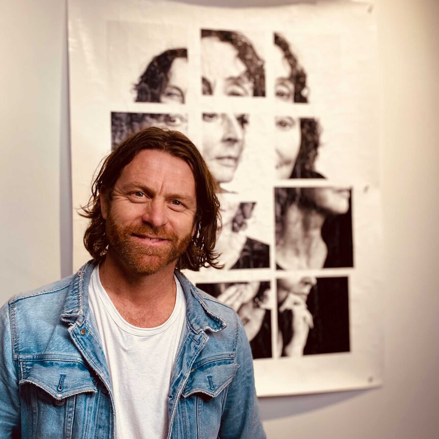 headshot of a man with beard, long hair and denim jacket standing in front of a fractured photo of a woman