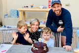 Cass Bennett with her husband and two kids smiling at a table with a big chocolate birthday cake.