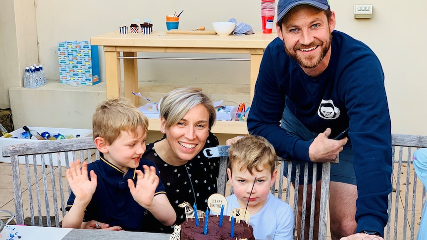 Cass Bennett with her husband and two kids smiling at a table with a big chocolate birthday cake.