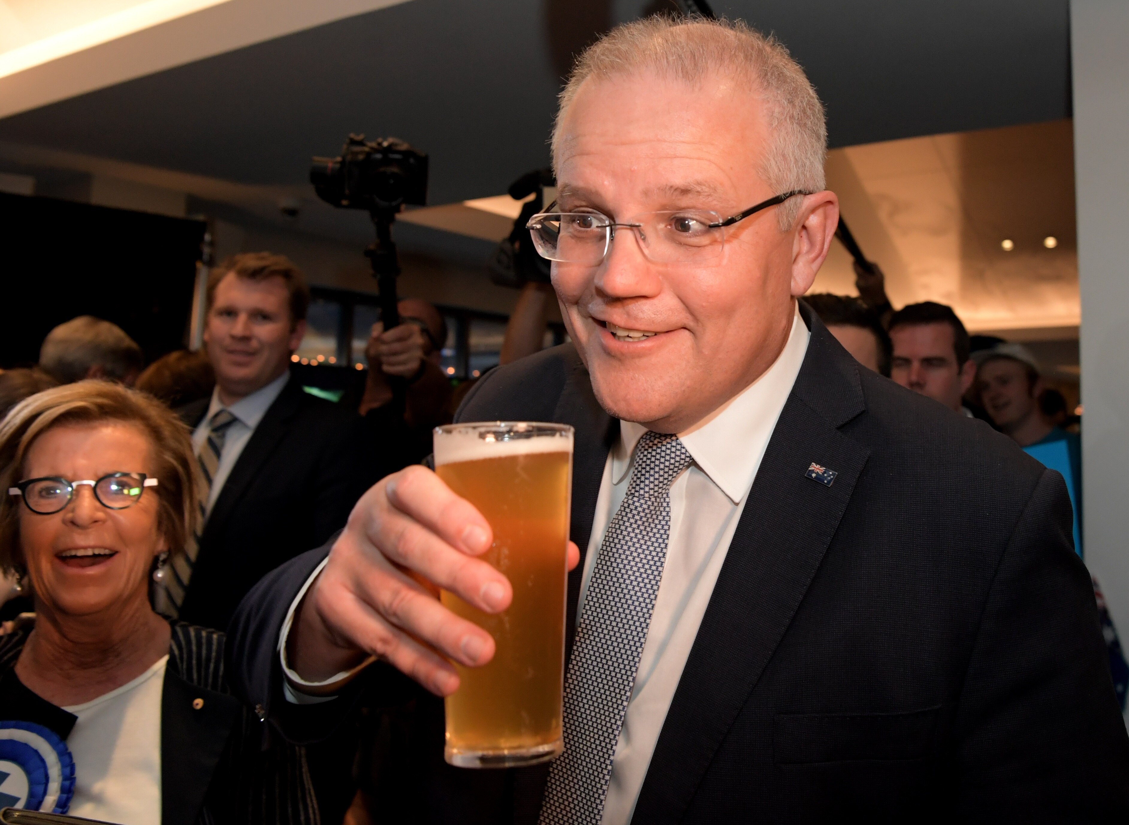 Scott Morrison holding a beer, smiling, as a crowd watches