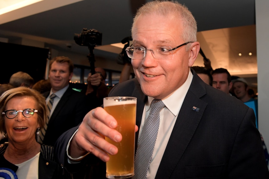 Scott Morrison holding a beer, smiling, as a crowd watches