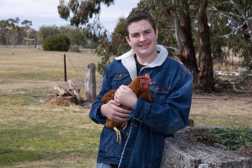 A teenager standing in a rural setting holding a chicken