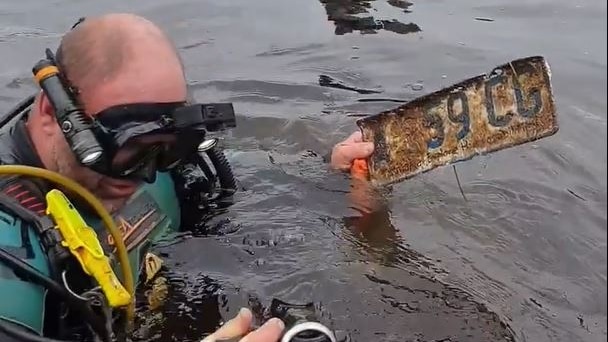 Diver emerges from river with car number plate.