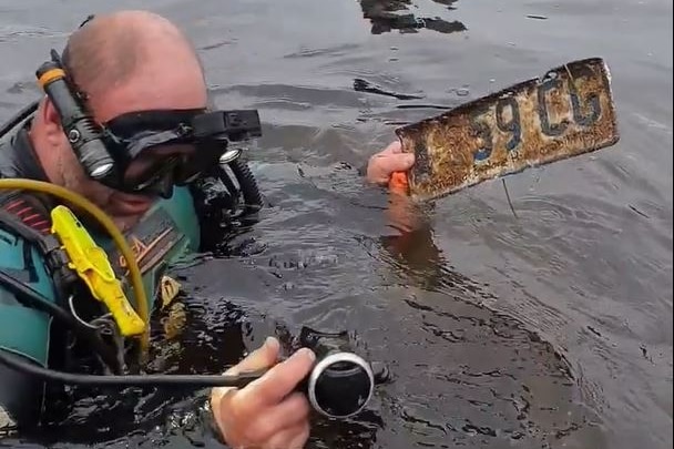 Diver emerges from river with car number plate.