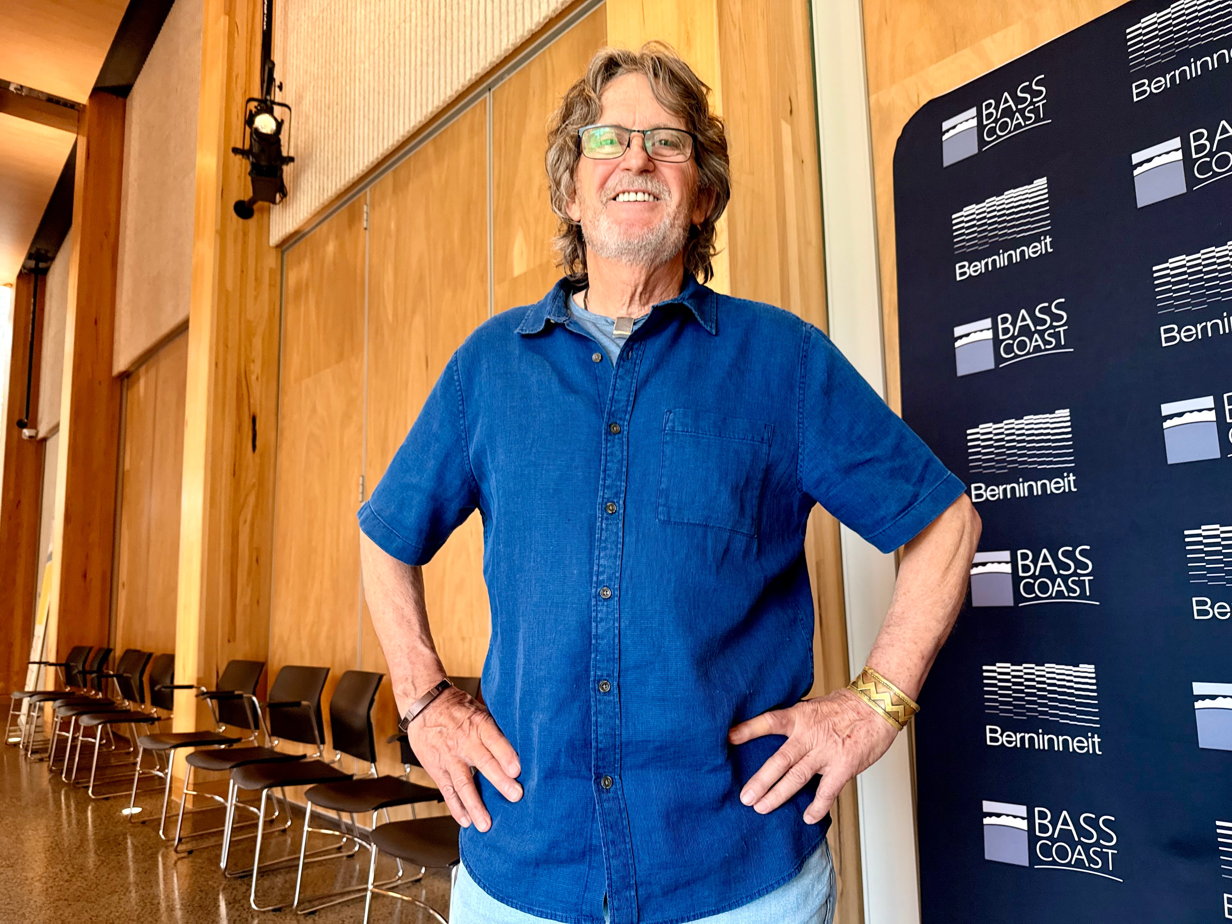Image of a man with long hair and a blue shirt with hands on his hips.