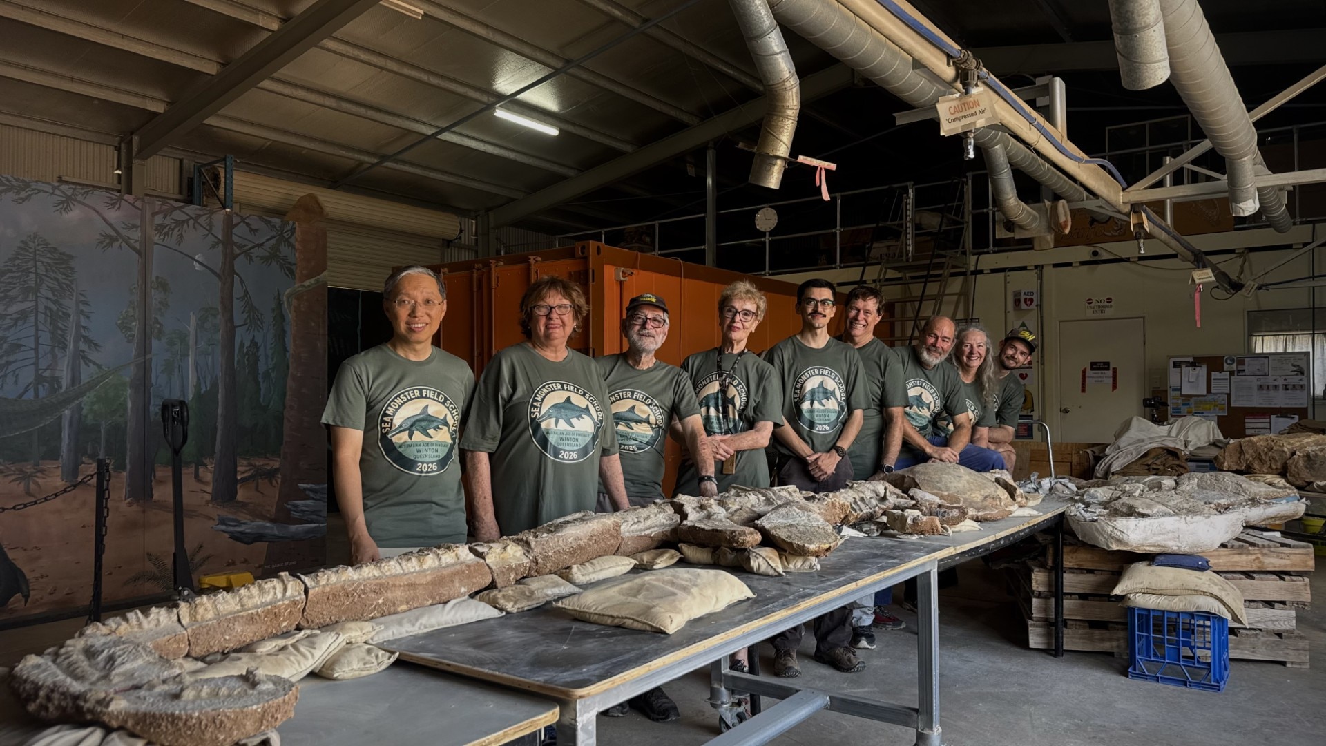 Nueve personas se encuentran ante una mesa con los restos de un antiguo ictiosaurio.