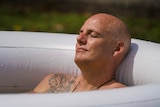 A man lays in a white ice bath with his eyes closed. He looks peaceful.