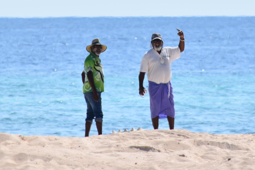 two men standing on a beach with the ocean behind them