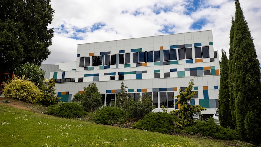 A white hospital building with multi-coloured panels and trees in front.