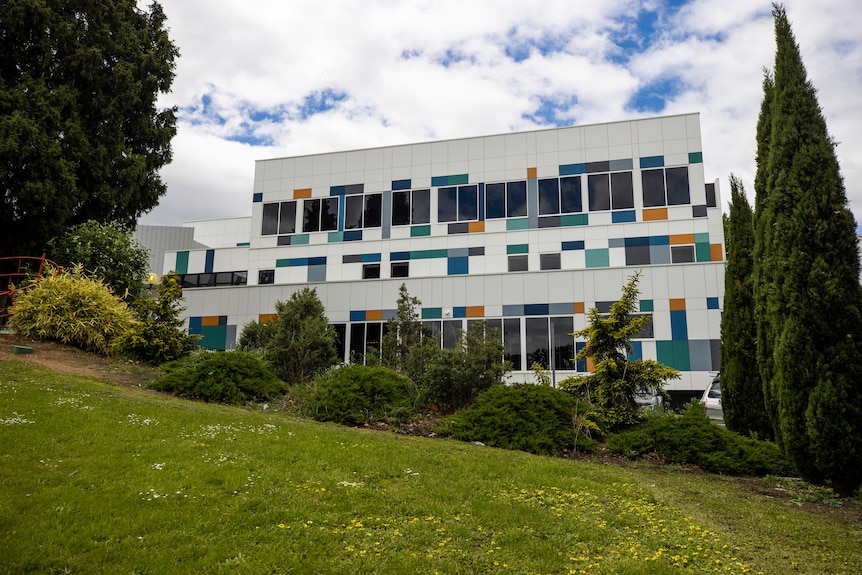 A white hospital building with multicolored panels and trees in front of it.