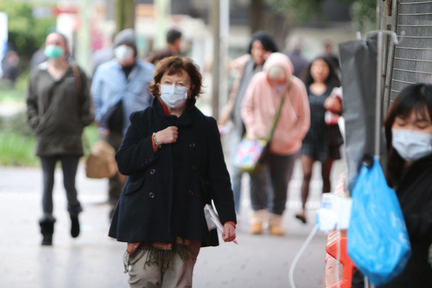 People of all ages walk outside wearing blue surgical masks.