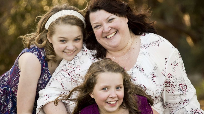 A smiling Mum with two younger daughters outside on grass