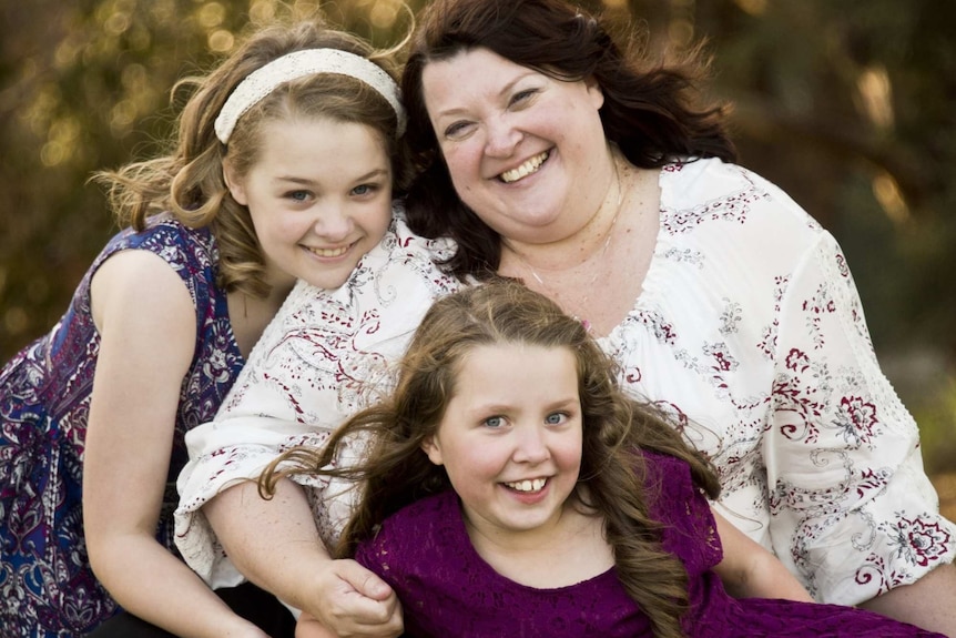 A smiling Mum with two younger daughters outside on grass