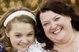 A smiling Mum with two younger daughters outside on grass